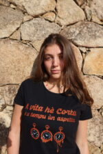 Femme portant T-shirt noir femme "A vita hè corta è u tempu ùn aspetta", vivre pleinement chaque instant, floqué d'horloges moles en cuivre à paillettes