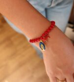 Personne portant le bracelet de perle de verre rouge avec 3 pampilles : médaille miraculeuse bleue marine, morceau de corail et petite croix rouge