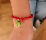 Personne portant le bracelet de perle de verre rouge avec 2 pampilles : médaille miraculeuse verte et morceau de corail