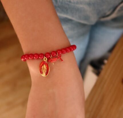 Personne portant le bracelet de perle de verre rouge avec 3 pampilles : médaille miraculeuse rouge, morceau de corail et petite croix rouge