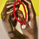 Bracelet en perles de verre rouges monté sur fil élastique, orné d’un morceau de corail naturel, d’une petite croix rouge et d’une médaille représentant la Madonuccia, symbole de la tradition corse et de la culture méditerranéenne.