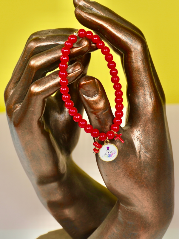 Bracelet en perles de verre rouges monté sur fil élastique, orné d’un morceau de corail naturel, d’une petite croix rouge et d’une médaille représentant la Madonuccia, symbole de la tradition corse et de la culture méditerranéenne.