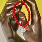 Bracelet Madonuccia rouge à 2 pampilles en perles de verre rouges, orné d’un fragment de corail naturel et d’une médaille représentant la Madonuccia, symbole de la tradition corse et de la culture méditerranéenne.