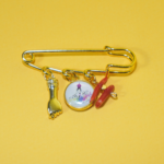 Broche artisanale à trois pampilles comprenant une médaille de la Madonuccia, un bras doré protecteur et un morceau de corail naturel, bijou L'Oru.