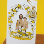 Carte médaille de Saint Joseph en acier inoxydable, illustrée avec un dessin exclusif pour L'Oru, représentant San Ghjisè avec une médaille recto-verso attachée à la carte.