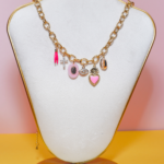 Collier en plaqué or avec pampilles roses : corne, médaille Vierge, croix en strass, œil protecteur, cœur ex-voto et cauri