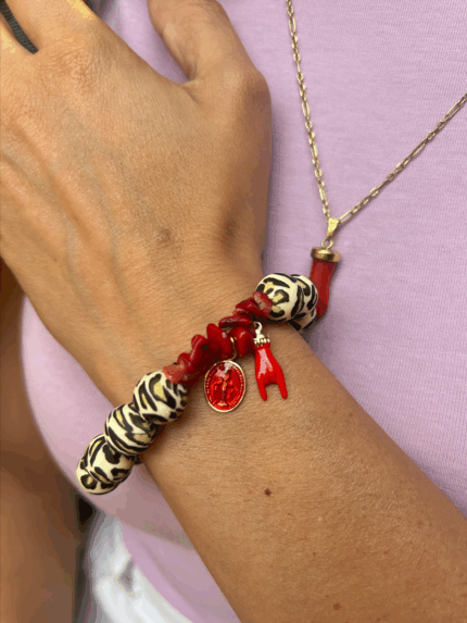 Bracelet léopard & corail porté au poignet, avec perles imprimées, corail rouge, médaille miraculeuse et corne protectrice. Style affirmé et méditerranéen.
