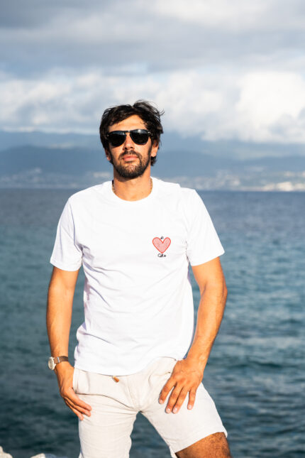 Homme de pied portant le tee-shirt blanc brodé Di Core, cœur rouge brodé visible côté cœur, coupe droite et look sobre