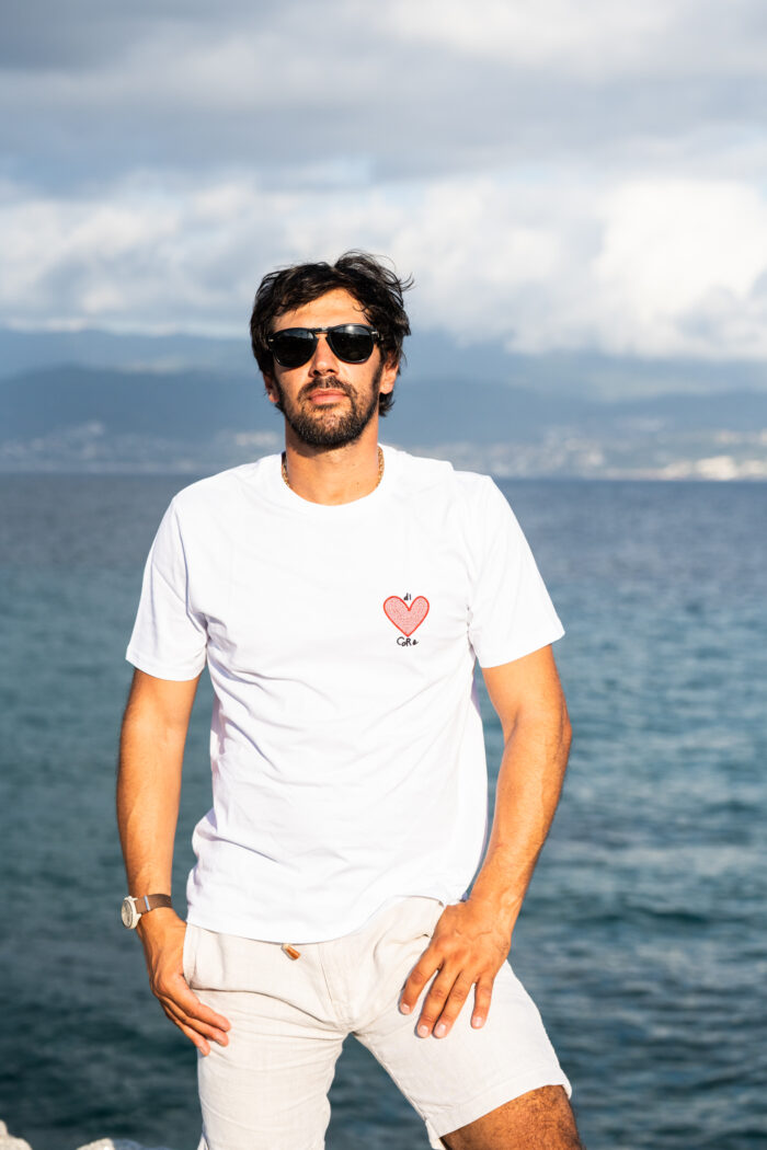Homme de pied portant le tee-shirt blanc brodé Di Core, cœur rouge brodé visible côté cœur, coupe droite et look sobre