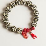 Bracelet en perles silicone motif léopard avec fragments de corail rouge, médaille miraculeuse rouge et corne protectrice, inspiré des traditions corses.