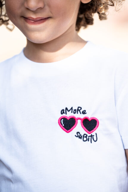 Enfant portant le tee-shirt brodé Amore Subitu blanc, message humoristique avec lunettes en forme de cœur, coupe unisexe, t-shirt blanc en coton