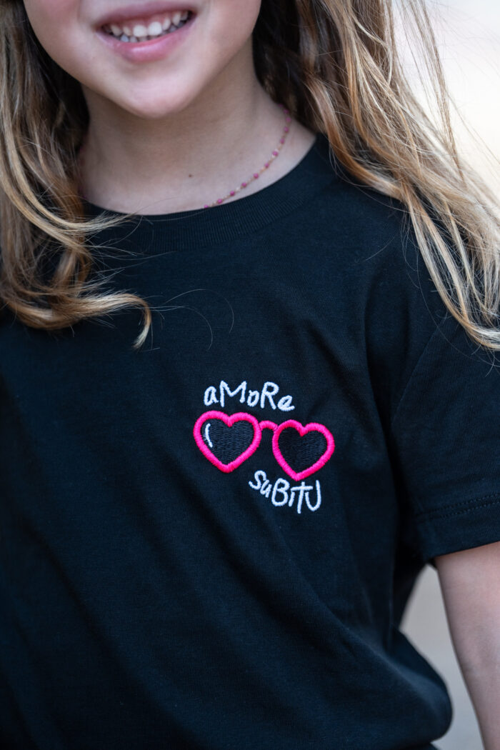 Enfant portant le tee-shirt brodé Amore Subitu noir, message humoristique avec lunettes en forme de cœur, coupe unisexe, t-shirt blanc en coton