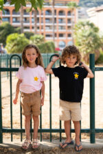 Enfants en pied portant un tee-shirt brodé Capu ind’e stelle, message poétique et étoile jaune, en noir et en rose