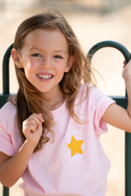 Enfant portant un tee-shirt brodé rose Capu ind’e stelle avec étoile jaune sur la poitrine, coupe unisexe et tissu 100 % coton, coloris noir