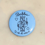 Badge bleu avec l'inscription Babbu, u rè di core, toute en finesse
